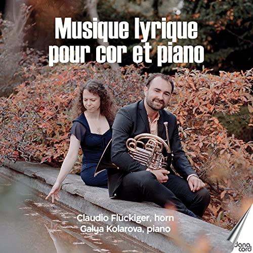 Musicians with a French horn and sheet music by a waterway.