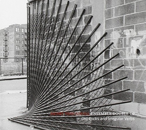 A black-and-white image of a metal fence with sharp bars against a brick wall.