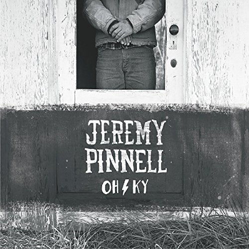 Black and white album cover with man standing in a doorway, artist and title text below.