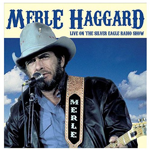 Merle Haggard in a cowboy hat singing into a microphone with a guitar.