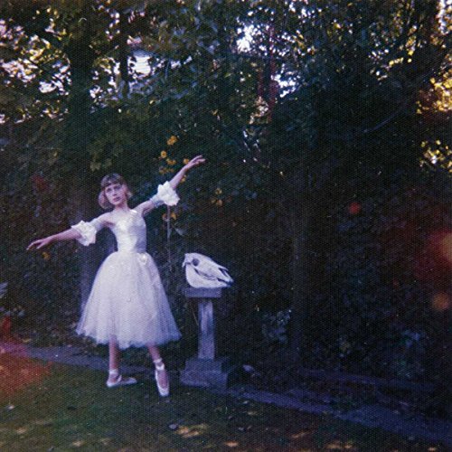 A woman in a white dress stands beside a birdbath in a lush, green outdoor setting.