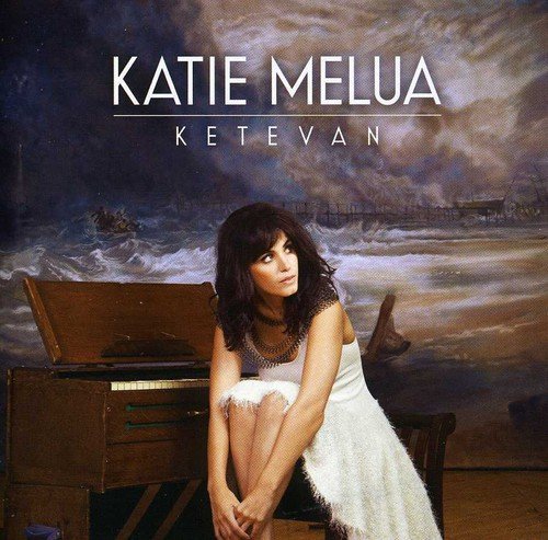 "Katie Melua sitting beside a piano, in a white dress, with a stormy sea backdrop."