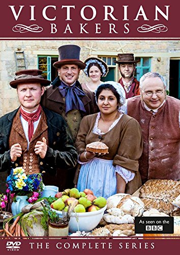 Five people in Victorian-style clothing pose behind a table filled with bread and fruit.