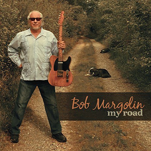 Man holding guitar stands on a forest path with a dog lying behind him.