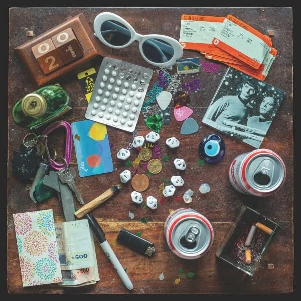 Album cover with scattered personal items: sunglasses, pills, tickets, and photos.