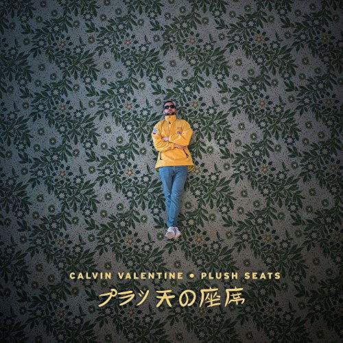 Man in yellow jacket and blue jeans standing against a floral wallpaper background.