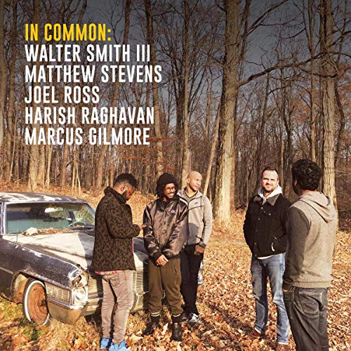 "Album cover featuring five men standing around an old car in a wooded area."