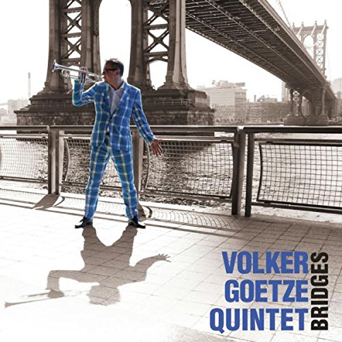 "Man in blue plaid suit playing trumpet on a bridge walkway."