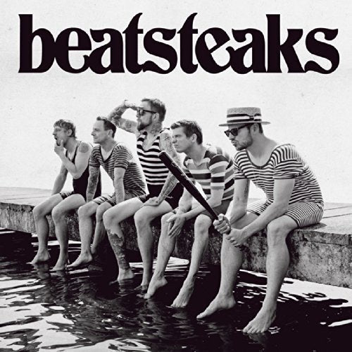 The image is a black-and-white album cover featuring six men sitting on a stone ledge. The alt text for this image could be: "Black and white album cover with six men in striped shirts."