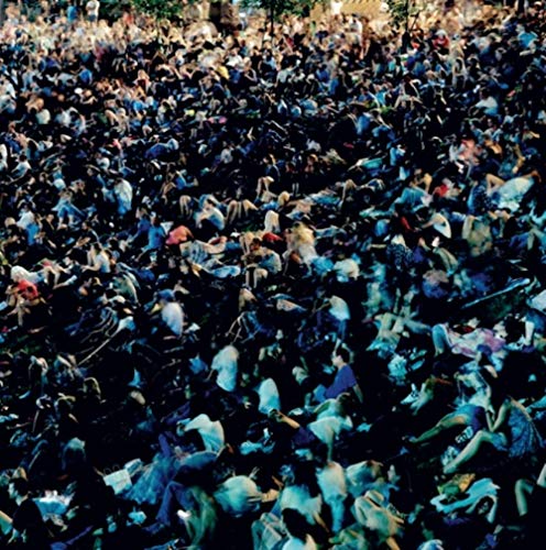 A dense crowd of people, mostly seated, fills the image, illuminated by stage lighting.