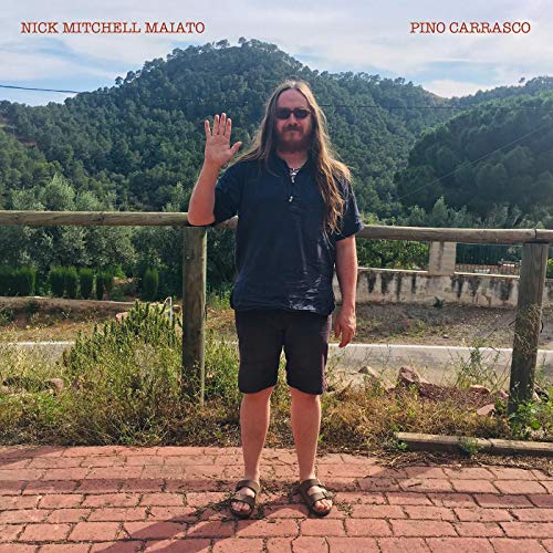 The image depicts a man standing on a brick path, waving, with a mountainous background.