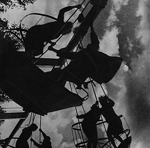 "Black and white image of silhouetted people on a spinning carnival ride against a cloudy sky."