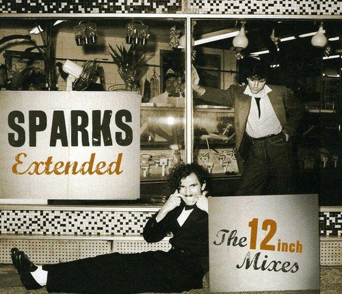 "Album cover with two men in suits, one sitting, one standing, in front of a storefront."