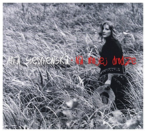 Black and white photo of a woman with a guitar in a field.