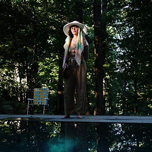 A woman in a white hat and scarf stands by a pool in woods.