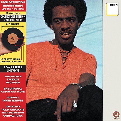 "Johnny Guitar holding a vinyl record, wearing an orange shirt, against a blue background."