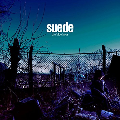 The image is a vinyl record cover for "Suede - The Blue Hour". Here is a concise description of the image in 15 words or less: Man kneeling by a chain link fence under a blue-toned, dusk sky.