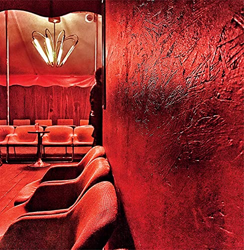 Red room interior with a chandelier and seated figures.