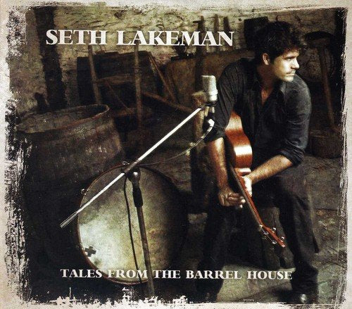 Seth Lakeman holding a violin, seated beside a large drum in a rustic room.