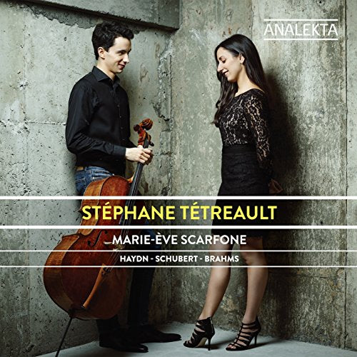 A man with a cello stands facing a woman in a black dress.