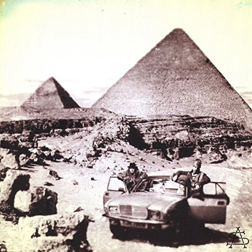 The image depicts a vintage car with people near the pyramids. #### Alt text: "Vintage convertible car with people near the pyramids in a sepia-toned image."