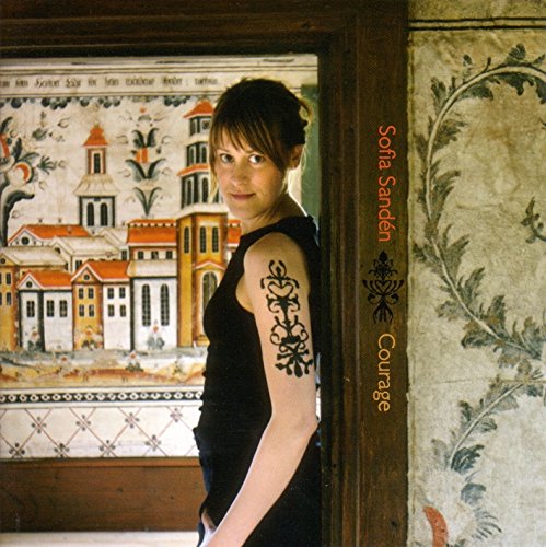Woman in black dress with tattoos stands beside a wooden frame with text "Sofia Sanden Courage".