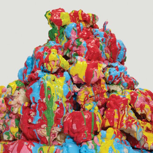 The image depicts a vibrant, abstract sculpture with red, blue, and yellow paint splatters. For accessibility purposes, a concise alt text could be: "Multicolored abstract sculpture with red, blue, and yellow paint splatters."