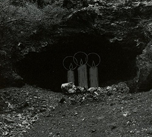 Black and white image of three lit candles inside a dark cave.