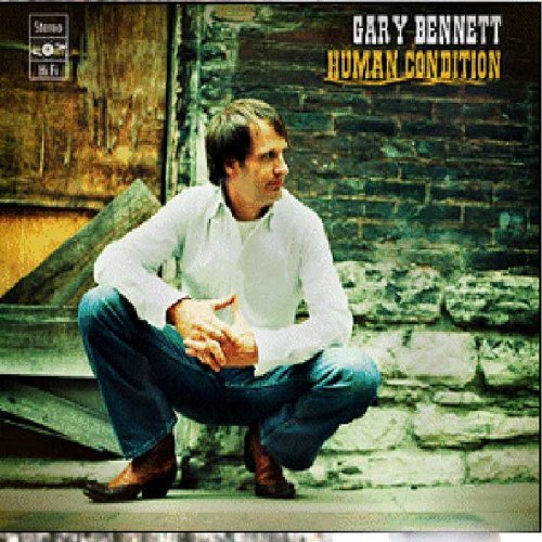 Album cover with man crouching, wearing white shirt and jeans, against a brick wall.
