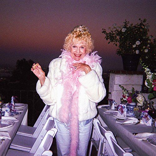 Woman with curly hair and a feather boa stands outdoors.