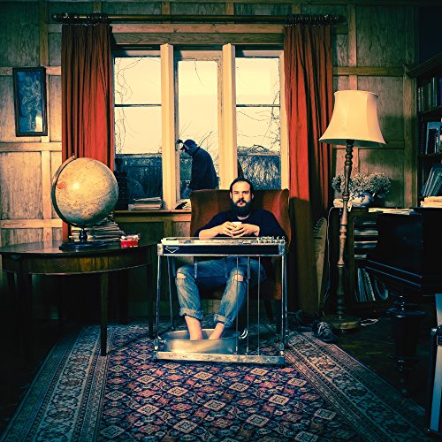 "Man sitting in a clear box in a dimly lit, wood-paneled room."