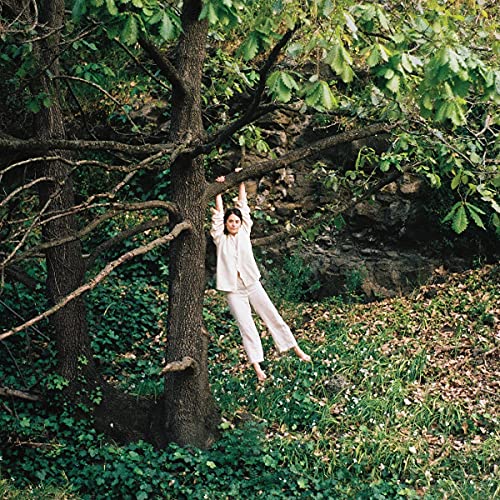 Woman in light clothing hangs from a tree branch in a forest.