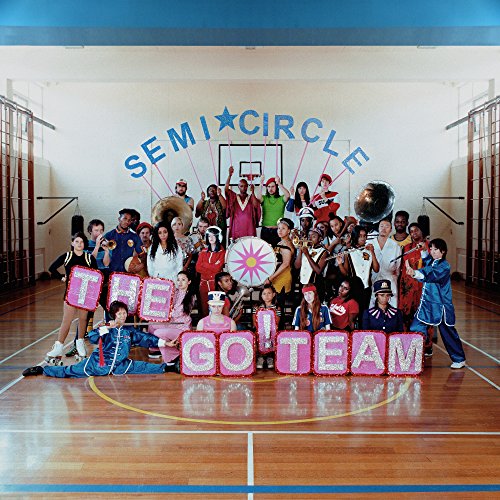 Large group posing with instruments and signs in a gymnasium.