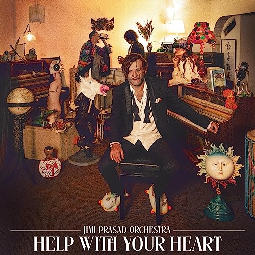 A man in a tuxedo sits on a piano bench surrounded by eclectic props.