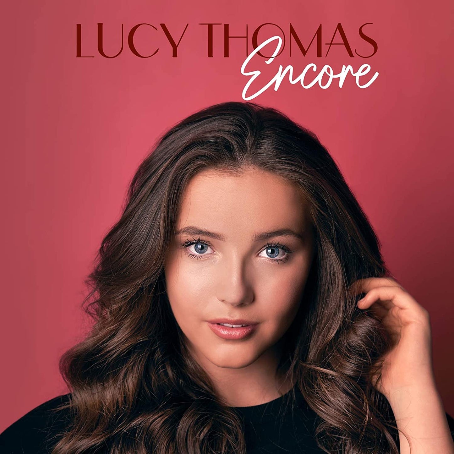 The image is a portrait of a woman with long brown hair against a red background. Alt text: Woman with long brown hair on red background, titled "Lucy Thomas Encore".