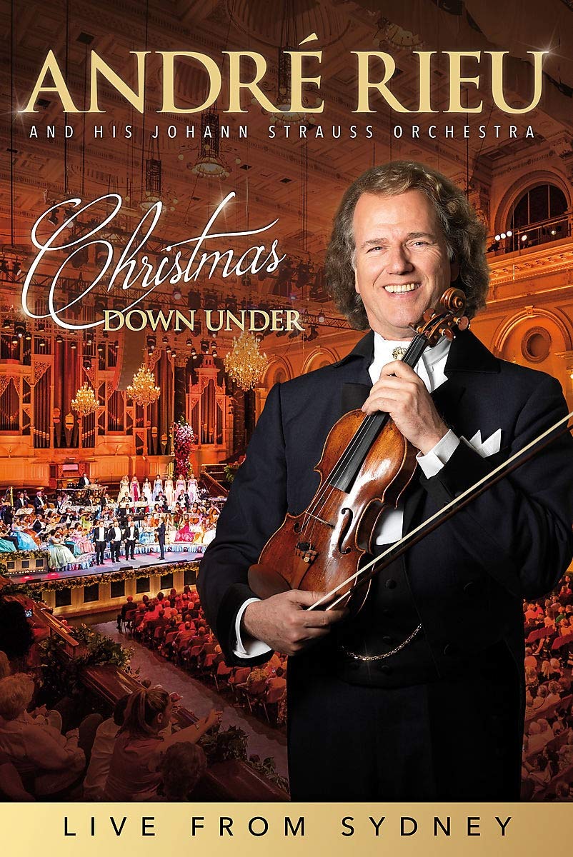 "Man in a tuxedo holding a violin, with an orchestra in the background."