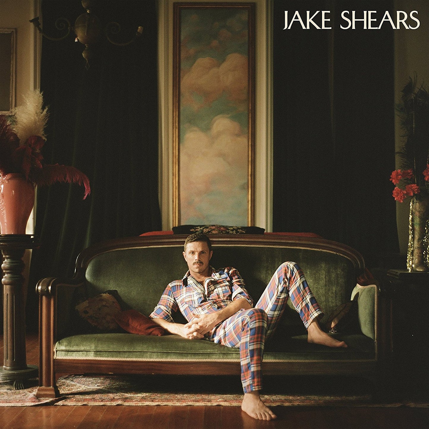 "Album cover featuring a man lounging on a green sofa, wearing plaid pajamas."