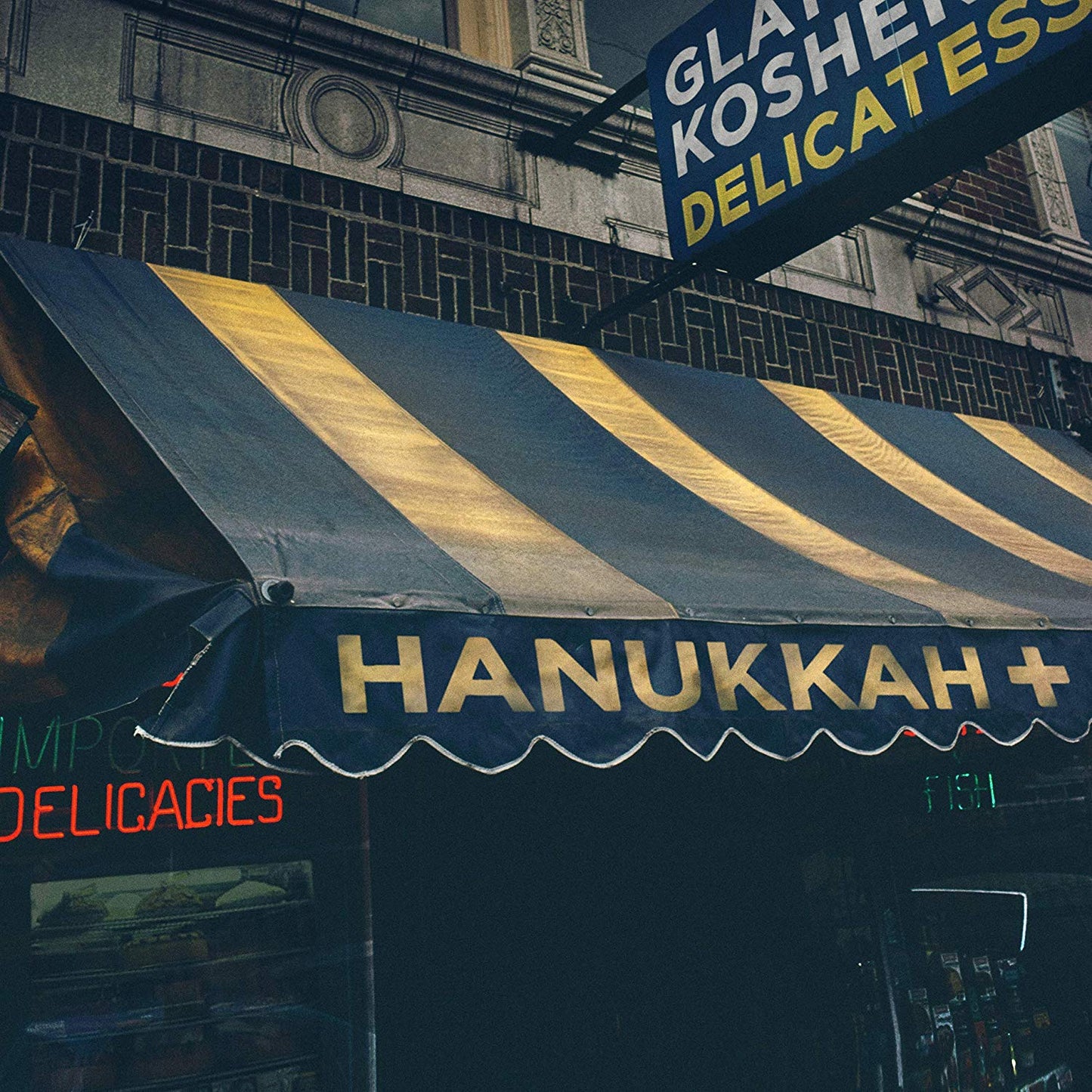 The image shows a storefront with a black and gold striped awning and a sign that reads "HANUKKAH +". The alt text for this image could be: "Storefront with black and gold striped awning, 'HANUKKAH +' sign."