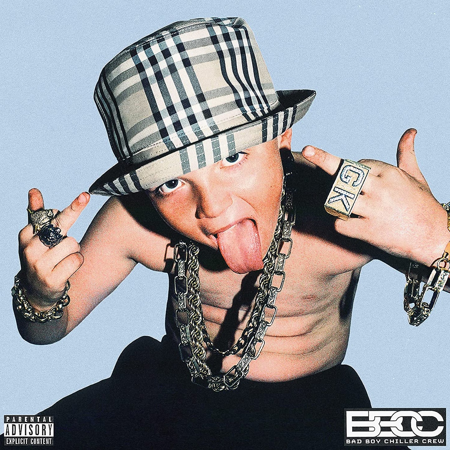 Young man in a hat and gold jewelry sticks tongue out.