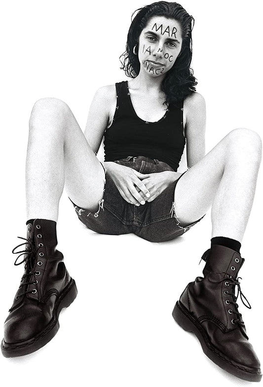 Black and white portrait of PJ Harvey seated, with writing on her face.