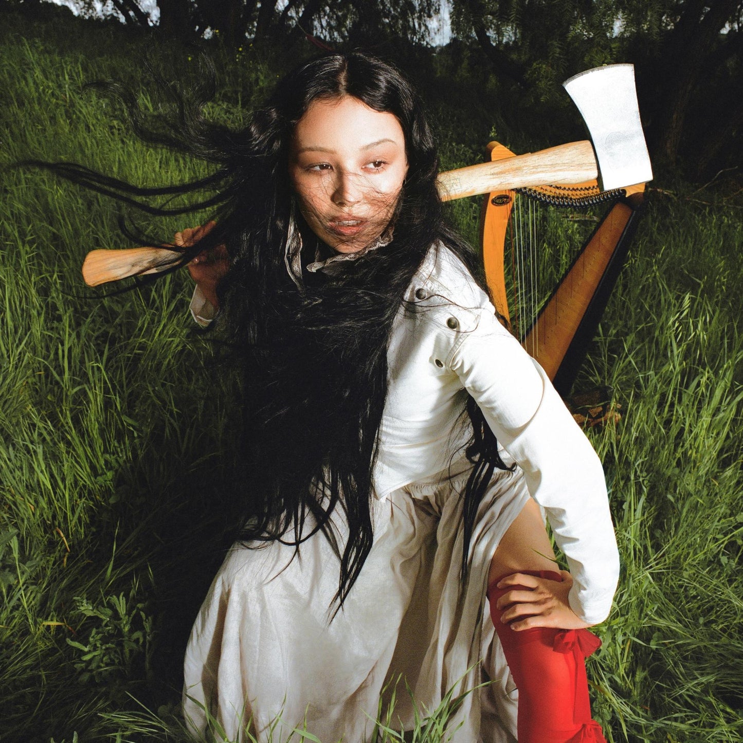 Luna Li in a white dress holds an axe and harp in tall grass.