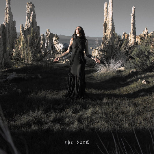 Woman in black dress stands in a desolate, rocky landscape.