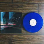 Blue vinyl record and album cover with blurred city lights.