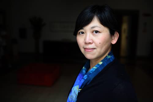 Portrait of a woman with dark hair, wearing a blue scarf and black jacket.