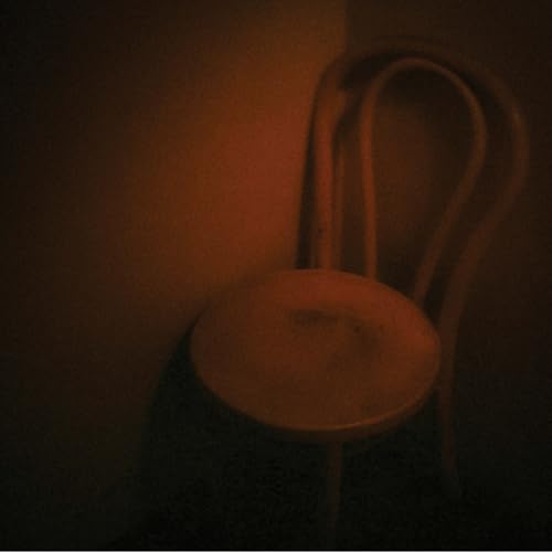 Dark, moody image of a wooden chair against a warm, reddish wall.
