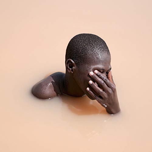 Man submerged in milky water, covering face with hands.
