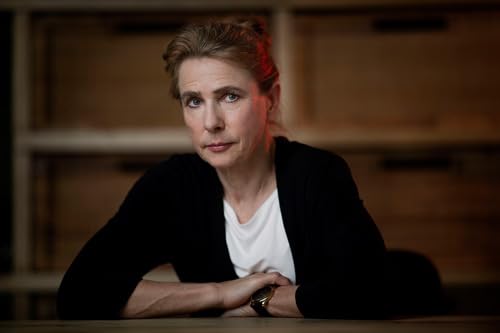 Woman with short brown hair, wearing black jacket, looks at viewer.