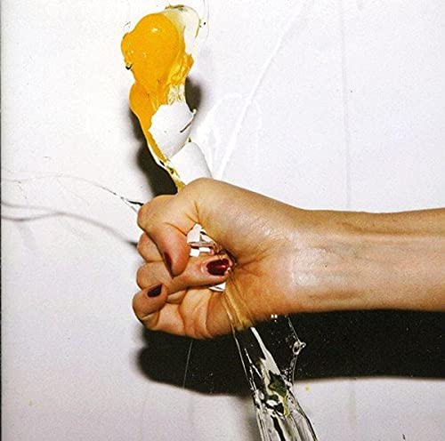 Hand holding a cracked egg with yolk running down a white surface.