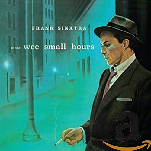 Frank Sinatra in a fedora and suit stands on a blue-lit city street.