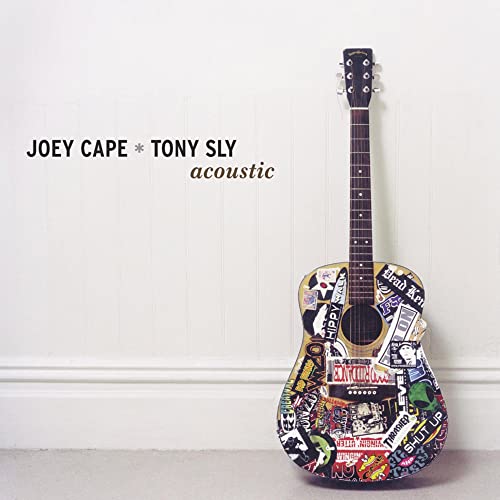 Sticker-covered acoustic guitar against a white paneled wall.